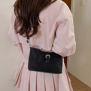 Detail of minimalist black crossbody bag with silver buckle worn over pink trench coat