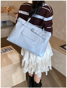 Detail view of light blue leather tote bag with decorative strap and metal buckle