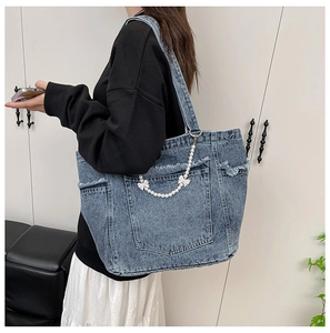 Detail view of large denim tote bag with frayed edges and pearl bow chain decoration
