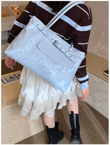 Detail of light blue tote bag with silver eyelets and buckle worn by a model in a cozy room
