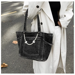 Close-up of black denim tote bag with frayed edges and decorative pearl chain bow