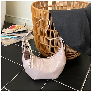 Detail of light pink patent leather shoulder bag with crescent shape and chic charms