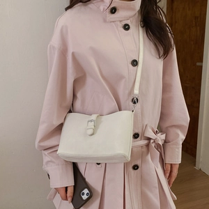 Detailed view of cream leather shoulder bag with silver buckle worn with a trench coat