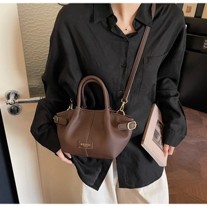 Detailansicht der braunen Lederhandtasche mit Textur und goldfarbenem Logo-Emblem