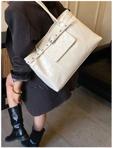 Detail of cream tote bag showing decorative strap with metal buckle and leather texture