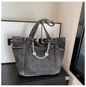 Detail of grey washed denim tote bag featuring frayed pockets and a pearl bow chain charm