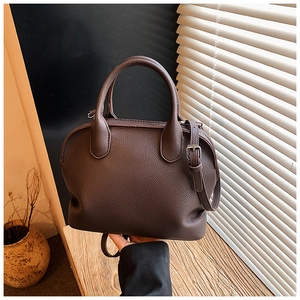Close-up of dark brown lychee leather Boston bag with circular handles and shoulder strap