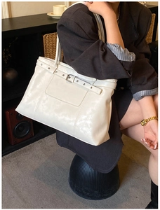 Detail of white leather tote bag with metal buckle on a dark blazer outfit