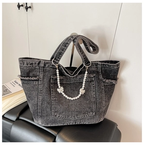 Detail of washed denim tote bag featuring decorative pearl chain and bow accents