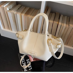 Detail einer cremefarbenen Handtasche aus Leder mit Lychee-Maserung und Goldbeschlägen