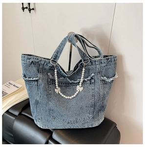 Detail of washed denim tote bag featuring frayed pockets and pearl bow decorative chain