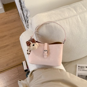 Pink underarm shoulder bag with cute teddy bear charm on a minimalist sofa