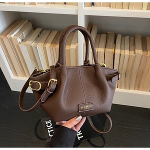 Detail einer braunen Handtasche aus Leder mit Lychee-Muster und goldenem Markenlogo