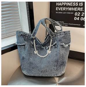 Close-up of denim tote bag featuring washed fabric, frayed edges, and pearl bow charm