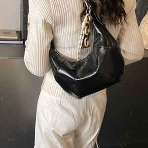 Detail of black crescent hobo bag featuring glossy leather and decorative chain handle