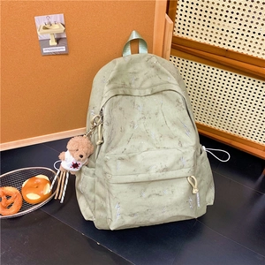 Detail view of a green lightning print backpack with a cute teddy bear charm