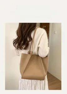 Detail of minimalist beige tote bag with litchi texture on a model's shoulder