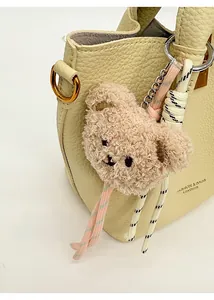 Close-up of fluffy brown bear bag charm with braided cords on a white leather handbag