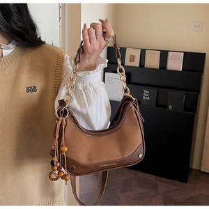 Gros plan du sac en daim marron avec chaîne dorée et pompon en perles de bois