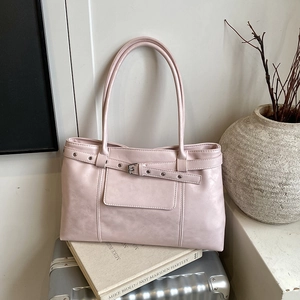 Minimalist light pink tote bag with metal buckle and long handles on a silver suitcase