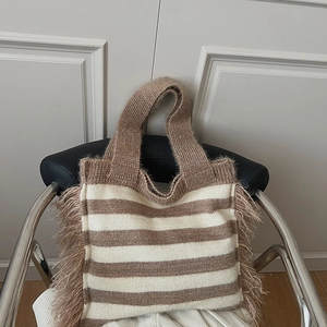 Detail of bohemian knitted tote bag featuring striped patterns and long fringes on leather chair