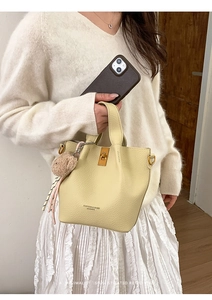 Detail view of cream bucket bag with lychee grain leather texture and gold hardware clasp