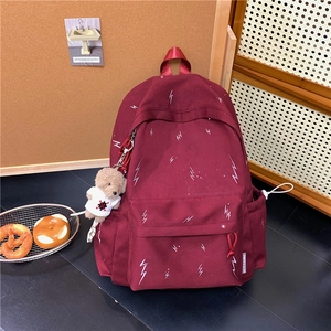 Detail view of burgundy canvas backpack with lightning patterns and a small bear keychain