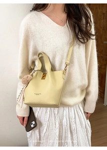 Close-up of cream leather bucket bag featuring a gold metal twist lock and plush charm