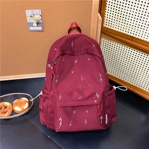 Detail view of burgundy backpack with lightning pattern showing side pockets and fabric label