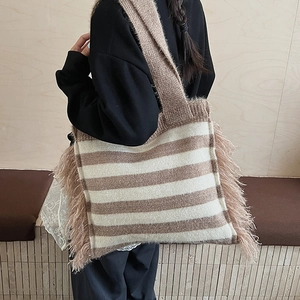 Close-up of a striped knitted tote bag with decorative plush fringe and woven texture