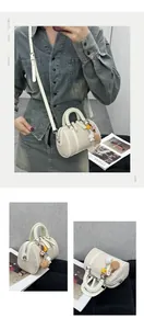 Detail of off-white Boston bag with litchi texture, dual handles and cute bear charm