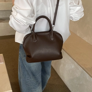 Detailed view of dark brown faux leather satchel bag worn as a crossbody on a model