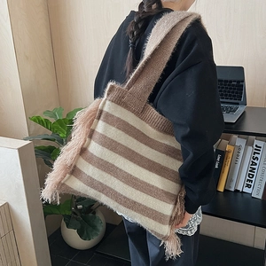 Detailed shot of striped knitted tote bag with boho tassels worn by model in home setting