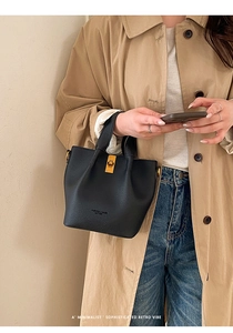 Detail of black lychee grain leather bucket bag with gold hardware and embossed text