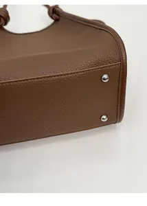 Detail view of brown pebbled leather bag base with silver anti-wear metal studs