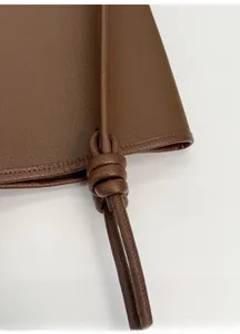 Macro shot of brown leather tote bag showing the textured finish and knotted strap detail
