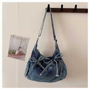 Detail of blue denim bow shoulder bag featuring washed fabric texture and silver hardware