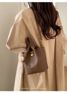 Detail of a brown leather bucket bag with gold twist lock and soft plush keychain charm