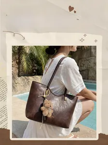 Detail of vintage brown PU leather tote bag featuring a cute plush bear pendant accessory