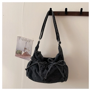 Close-up of black denim crossbody bag featuring drawstring bow details and metal buckle