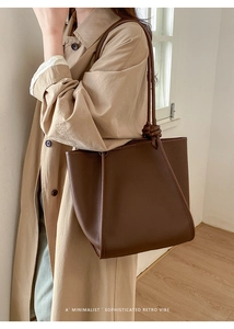 Detail of brown litchi pattern leather tote with knot-design strap on a tan trench coat
