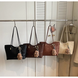 Detail of four PU leather tote bags in various colors with cute bear charms hanging on a rack