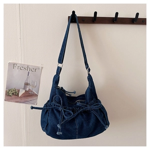 Detail of blue denim hobo bag featuring drawstring bow decoration and silver metal buckle