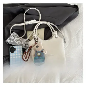 Close-up of white matte leather bucket bag with circular handles and plush bear charm