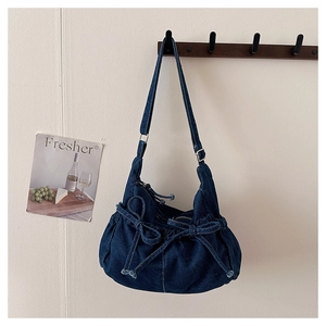 Detailed view of blue denim shoulder bag with bow accents and drawstring ruffles