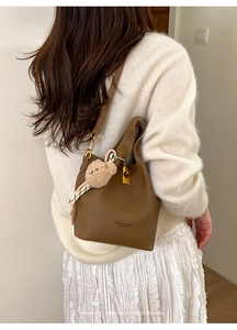 Detail view of brown litchi leather bucket bag with metal lock and cute bear charm