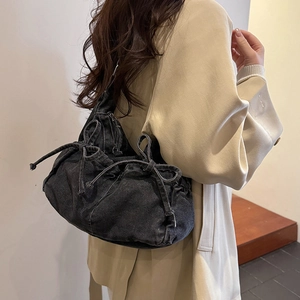 Detail of a black denim bow shoulder bag with drawstring closure and silver hardware details