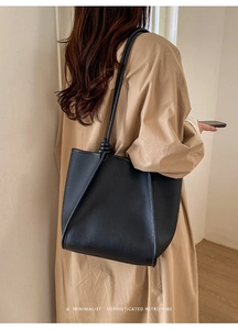 Close-up of black lychee-grain leather tote bag showing a side view with shoulder strap knot