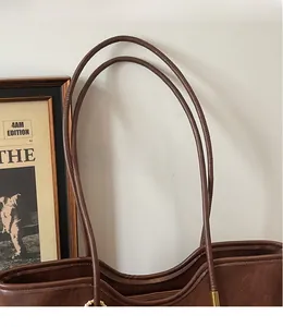 Detail view of the long cylindrical shoulder straps on a dark brown leather tote bag