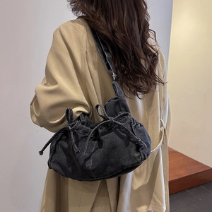 Detail of grey denim shoulder bag with bow accents worn over a beige trench coat